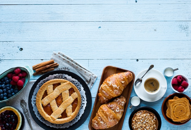 Bovenaanzicht van een houten tafel vol cakes, fruit, koffie, koekjes, kruiden en meer