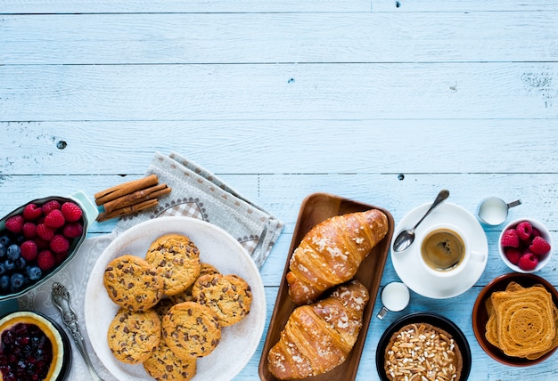 Bovenaanzicht van een houten tafel vol cakes, fruit, koffie, koekjes, kruiden en meer