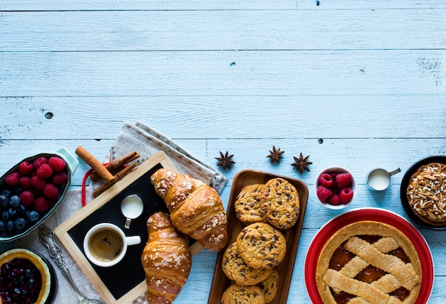 Bovenaanzicht van een houten tafel vol cakes, fruit, koffie, koekjes, kruiden en meer