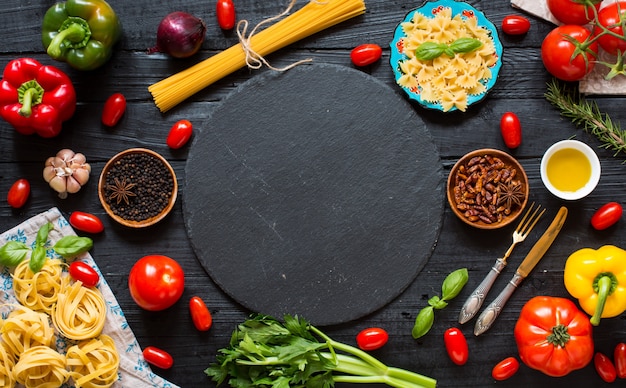 Bovenaanzicht van een houten tafel vol met Italiaanse pasta ingradients zoals paprika, tomaten, olijfolie, basi