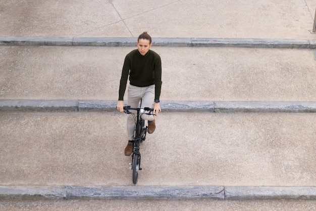 Bovenaanzicht van een jonge man op een fiets die de trap afgaat van zijn werkkantoor in het financiële district