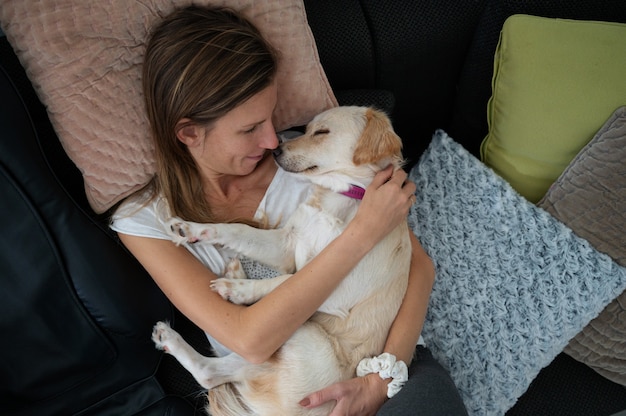 Bovenaanzicht van een jonge vrouw die knuffelt met haar schattige witte hond die op haar schoot slaapt.