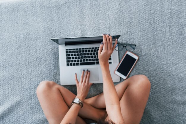 Bovenaanzicht van een jonge vrouw in casual kleding die alleen thuis zit met een laptop.