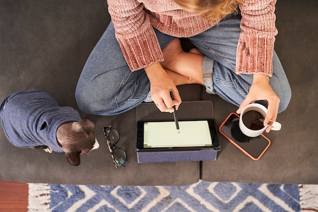 Bovenaanzicht van een jonge vrouw met behulp van digitale tablet zittend op een bank