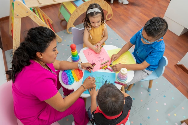 Foto bovenaanzicht van een kinderarts tekenen met 3 kinderen aan een tafel in haar kantoor