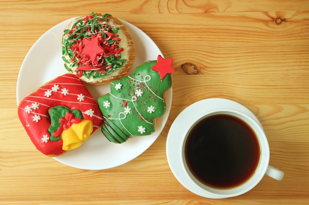 Bovenaanzicht van een kop warme koffie en een bord met kerstversierde snoepjes op houten tafel