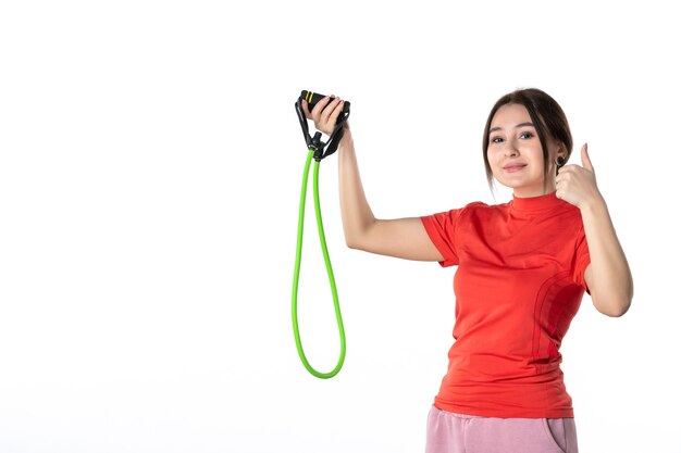 Bovenaanzicht van een lachende zelfverzekerde jonge vrouw die netjes haar haar verzamelt, gekleed in een oranje blouse en touw sportaccessoire vasthoudt en een goed gebaar maakt op witte achtergrond