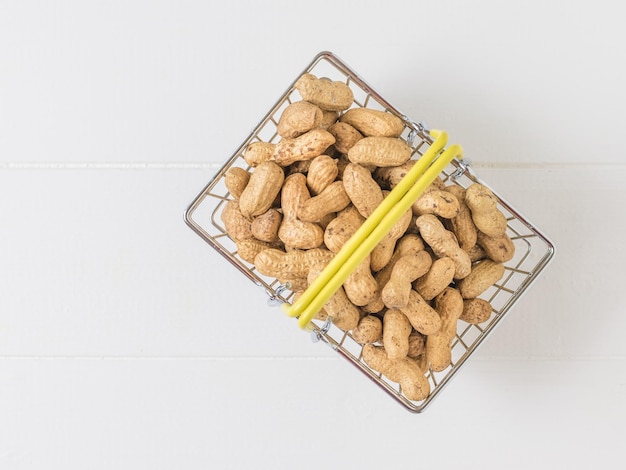 Bovenaanzicht van een mand met pinda's op een witte houten tafel