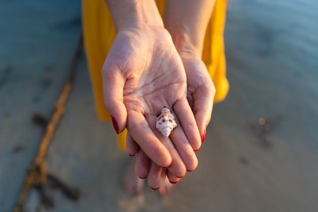 Bovenaanzicht van een meisje in een gele jurk met een zeeschelp in haar handen terwijl je in het water. Handen sluiten omhoog.