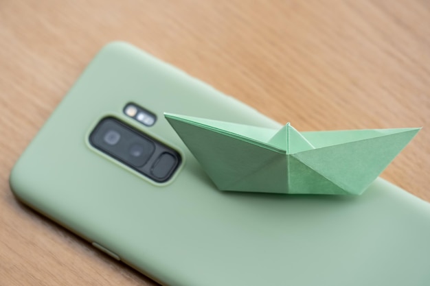 Bovenaanzicht van een mintgroene smartphone met een papieren bootje erop op een houten ondergrond