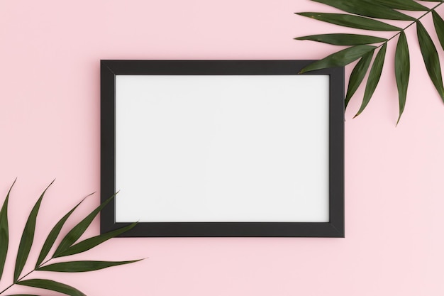 Bovenaanzicht van een mockup met zwart frame met palmbladdecoratie op een roze achtergrond Landschapsoriëntatie