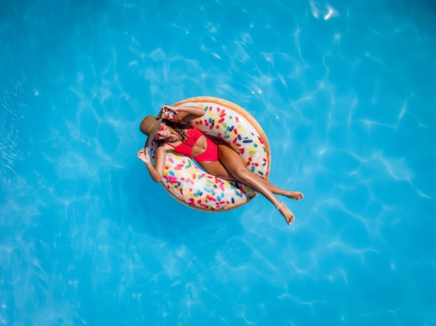Bovenaanzicht van een mooie jonge vrouw in zwembad zwemt op opblaasbare ring donut en heeft plezier op vakantie.