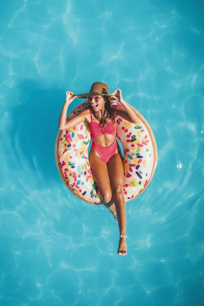 Bovenaanzicht van een mooie jonge vrouw in zwembad zwemt op opblaasbare ring donut en heeft plezier op vakantie.