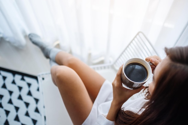 Bovenaanzicht van een mooie vrouw die 's ochtends thuis hete koffie drinkt in de slaapkamer