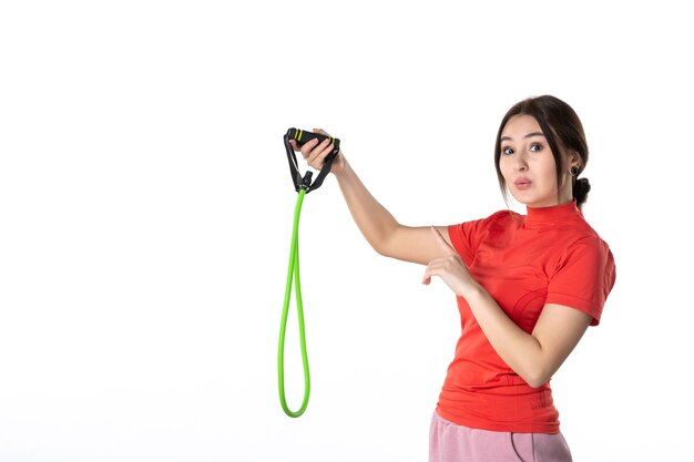 Bovenaanzicht van een nieuwsgierige jonge vrouw die netjes haar haar verzamelt, gekleed in een oranje blouse en touwsportaccessoire vasthoudt dat iets op een witte achtergrond wijst