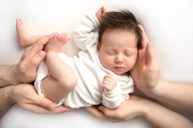 Bovenaanzicht van een pasgeboren babymeisje liggend in een witte overall in de armen van haar ouders Mooi portret van een klein meisje met gesloten ogen De handpalmen van de ouders houden het kind bij het lichaam