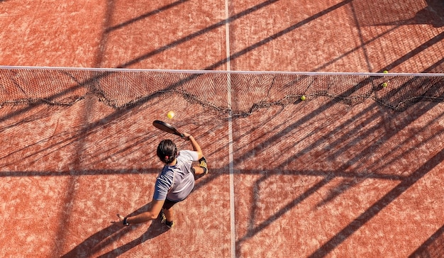 Bovenaanzicht van een professionele paddle-tennisser die de bal in de buurt van het net op een buitenbaan slaat.