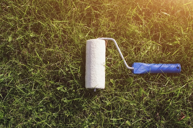 Bovenaanzicht van een verfroller met een blauw handvat, dat is een met gras begroeide strook schilderen met gazon als kleur.