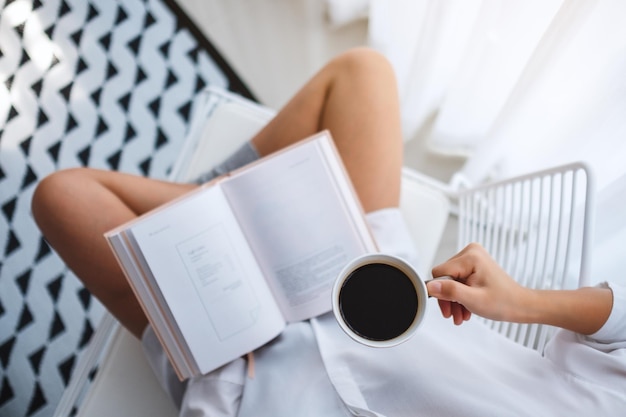 Bovenaanzicht van een vrouw die een boek leest en 's ochtends thuis warme koffie drinkt in de slaapkamer