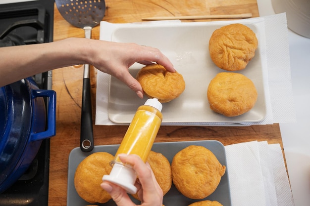 Bovenaanzicht van een vrouw die zelfgemaakte veganistische donuts maakt en ze vult met abrikozenjam