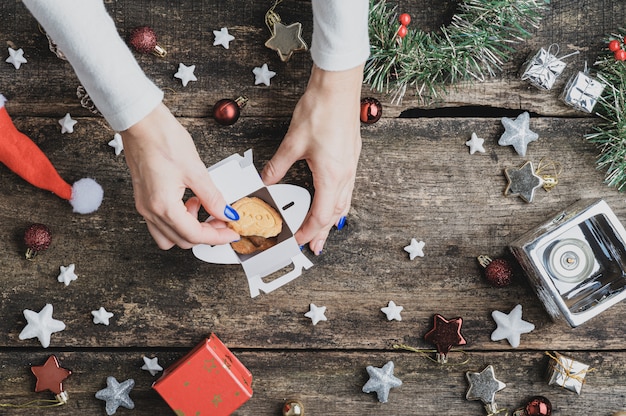 Bovenaanzicht van een vrouw vakantie koekjes plaatsen in mini geschenkdoos op rustieke houten bureau