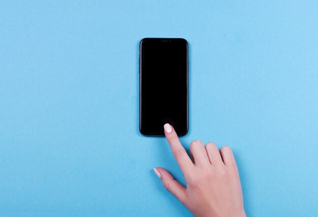 Bovenaanzicht van een vrouwenhand die iphone op blauwe achtergrond gebruikt