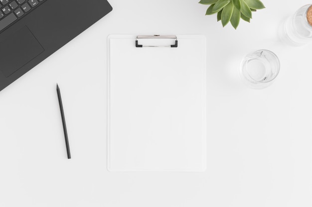 Bovenaanzicht van een wit klembordmodel met laptop voor werkruimteaccessoires en een vetplant op een witte tafel