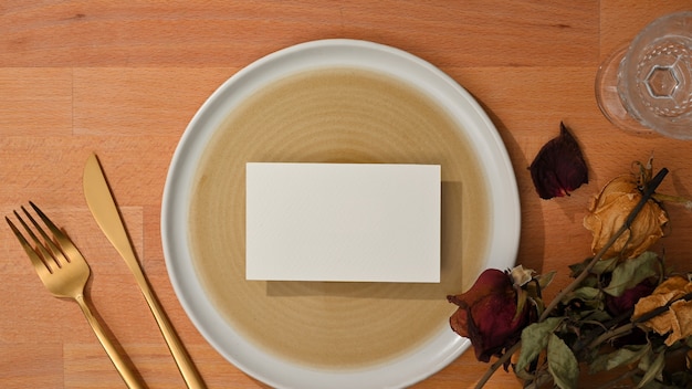 Bovenaanzicht van eetset met mock-up naamkaartje op mock-up keramische plaat en koperen vork en tafelmes