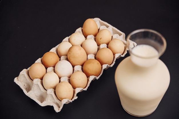 Bovenaanzicht van eieren in container en glas verse melk op donkere ondergrond.