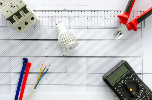 Foto bovenaanzicht van elektrische gereedschappen en materialen voor elektrisch systeem, tang, kabel, led-lamp, voltmeter en brekerbril op witte achtergrond