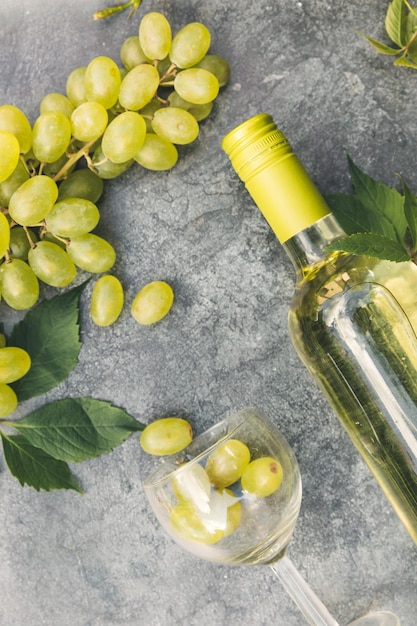 Bovenaanzicht van fles witte wijn groene wijnstok wijnglas en rijpe druif op vintage grijze stenen tafel achtergr...