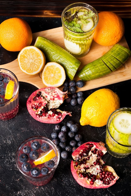 Bovenaanzicht van fruit, groenten en bessen naast glazen met detox water op donkere houten achtergrond