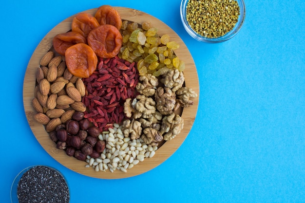 Bovenaanzicht van gedroogde abrikozen, rozijnen, gojibessen, noten, chiazaadjes en bijenpollen op de snijplank