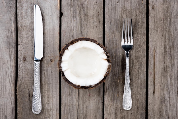 Bovenaanzicht van gehalveerde kokosnoot met vork en mes op houten tafelblad