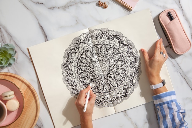 Bovenaanzicht van gekleurd mandala-kunstboek met kleurrijke markeringen, pen, roze etui en een kopje koffie