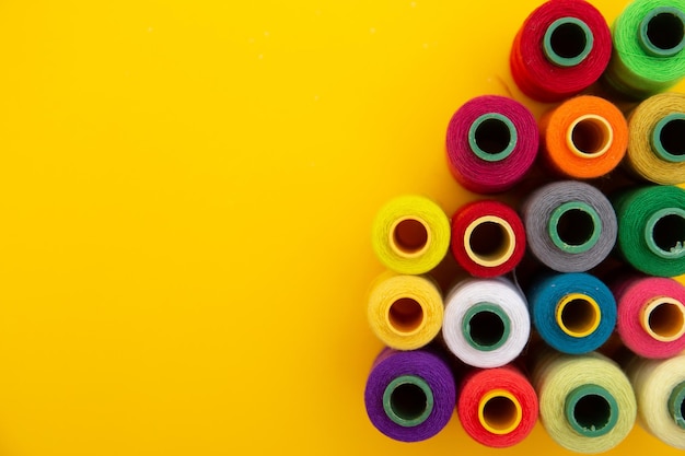 Bovenaanzicht van gekleurde draadspoelen op gele achtergrond, naaien, plaats voor tekst