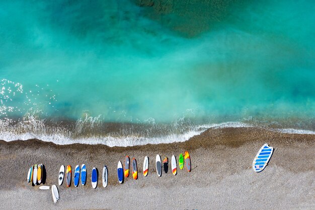Bovenaanzicht van gekleurde surfplanken chaotisch liggend op een kiezelstrand.