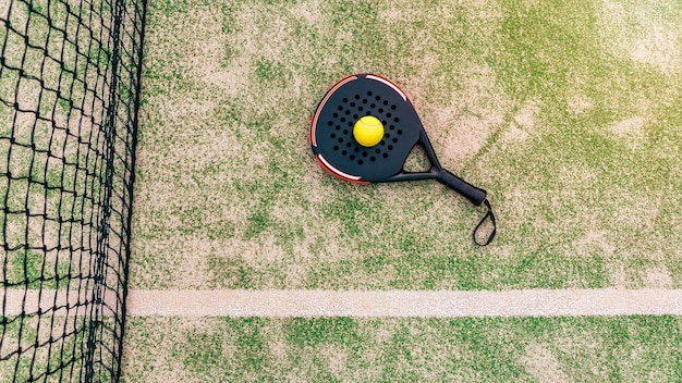 Bovenaanzicht van gele bal over padel tennisracket achter net in groene rechtbank