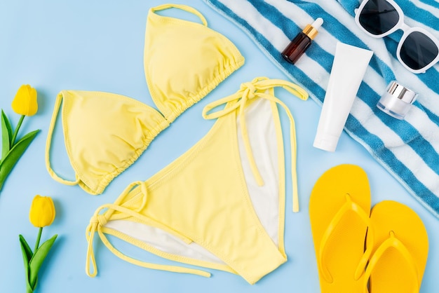 Bovenaanzicht van gele bikini en crème fles sandalen zonnebril met strand accessoires op de blauwe achtergrond zomertijd concept