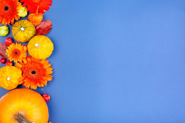 Bovenaanzicht van gele en oranje bloemen en pompoenen op blauwe achtergrond met kopie ruimte. Lege wenskaart voor creatief werk ontwerp. plat lag