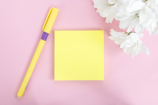 Bovenaanzicht van gele stickervellen met pen en bloemen Roze tafel