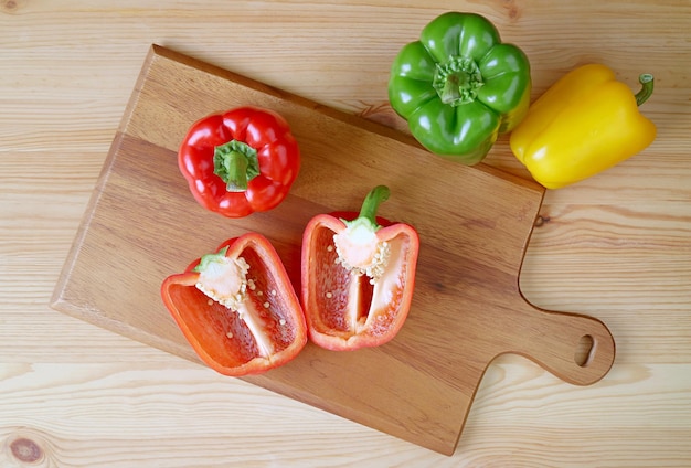 Bovenaanzicht van gesneden rode paprika op snijplank met driekleurige paprika's verspreid over