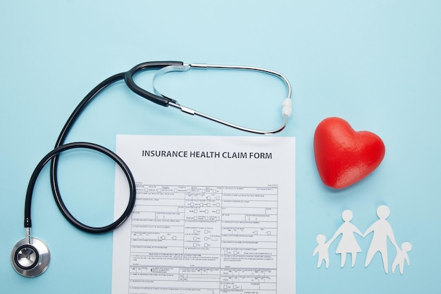 Bovenaanzicht van gezondheidsclaimformulier, papier gesneden familie, rood hartsymbool en stethoscoop op blauw