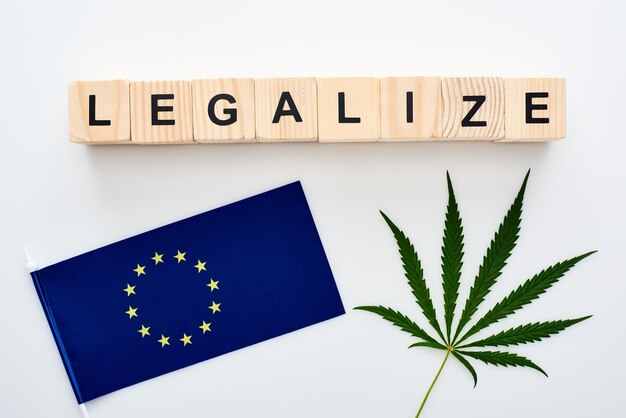 Bovenaanzicht van groen cannabisblad en legaliseer letters op houten kubussen bij de vlag van Europa op wit