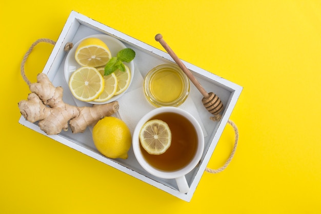 Bovenaanzicht van groene thee met citroen, honing en gember in het witte houten dienblad op het gele oppervlak