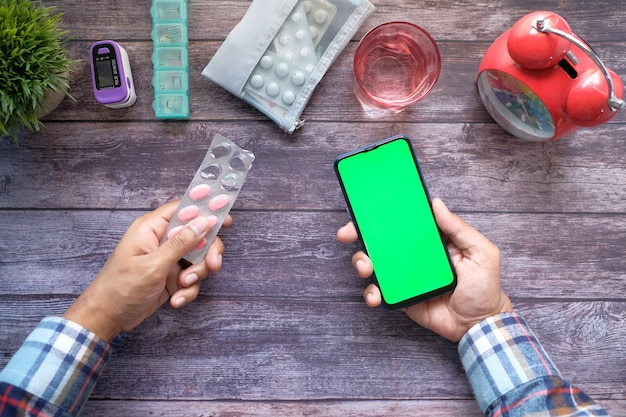 Bovenaanzicht van hand met blisterverpakkingen en slimme telefoon op tafel