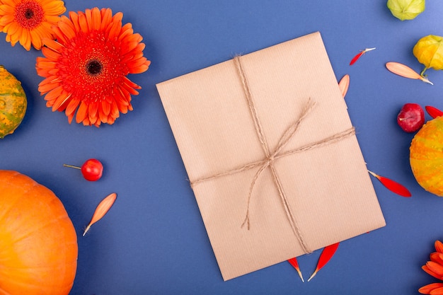 Bovenaanzicht van handgemaakte geschenkdoos met gele en oranje bloemen en pompoenen op blauwe muur Lege wenskaart voor creatief werk ontwerp. plat lag