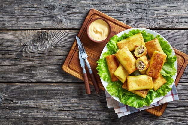 Bovenaanzicht van hartige crêpe broodjes met gemalen kippenvlees en champignonvulling geserveerd op een bedje van verse slablaadjes op een witte plaat