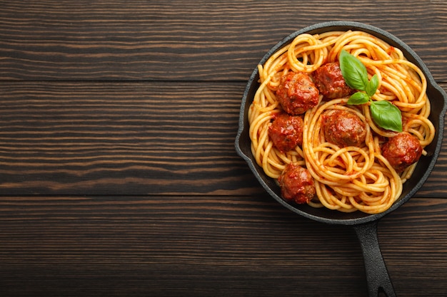 Bovenaanzicht van heerlijke pasta met gehaktballen, tomatensaus en verse basilicum in gietijzeren rustieke vintage pan geserveerd op snijplank, houten achtergrond. lekkere zelfgemaakte gehaktballen spaghetti, ruimte voor tekst