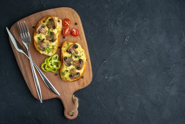 Bovenaanzicht van heerlijke snacks met verse champignons en bestek op houten snijplank aan de rechterkant op zwarte achtergrond